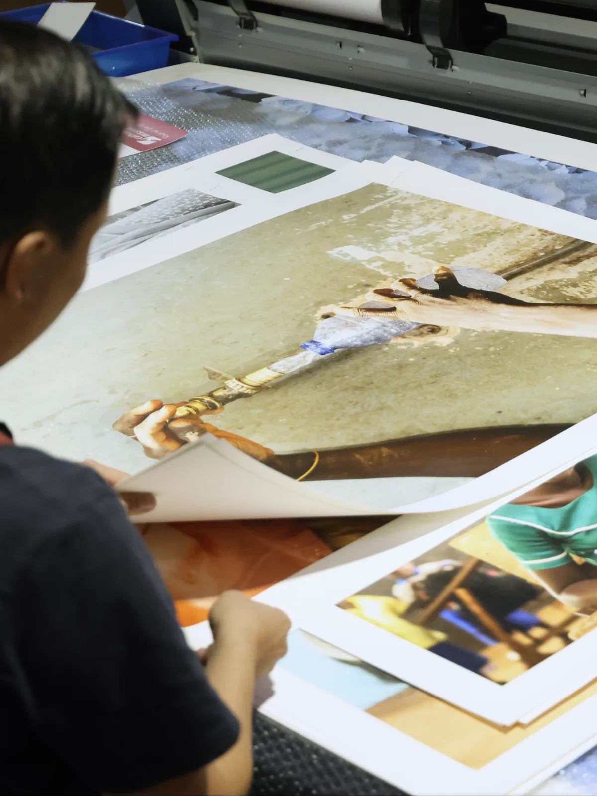A printer in the workshop sorting large printed photographs beside the wide-format printer