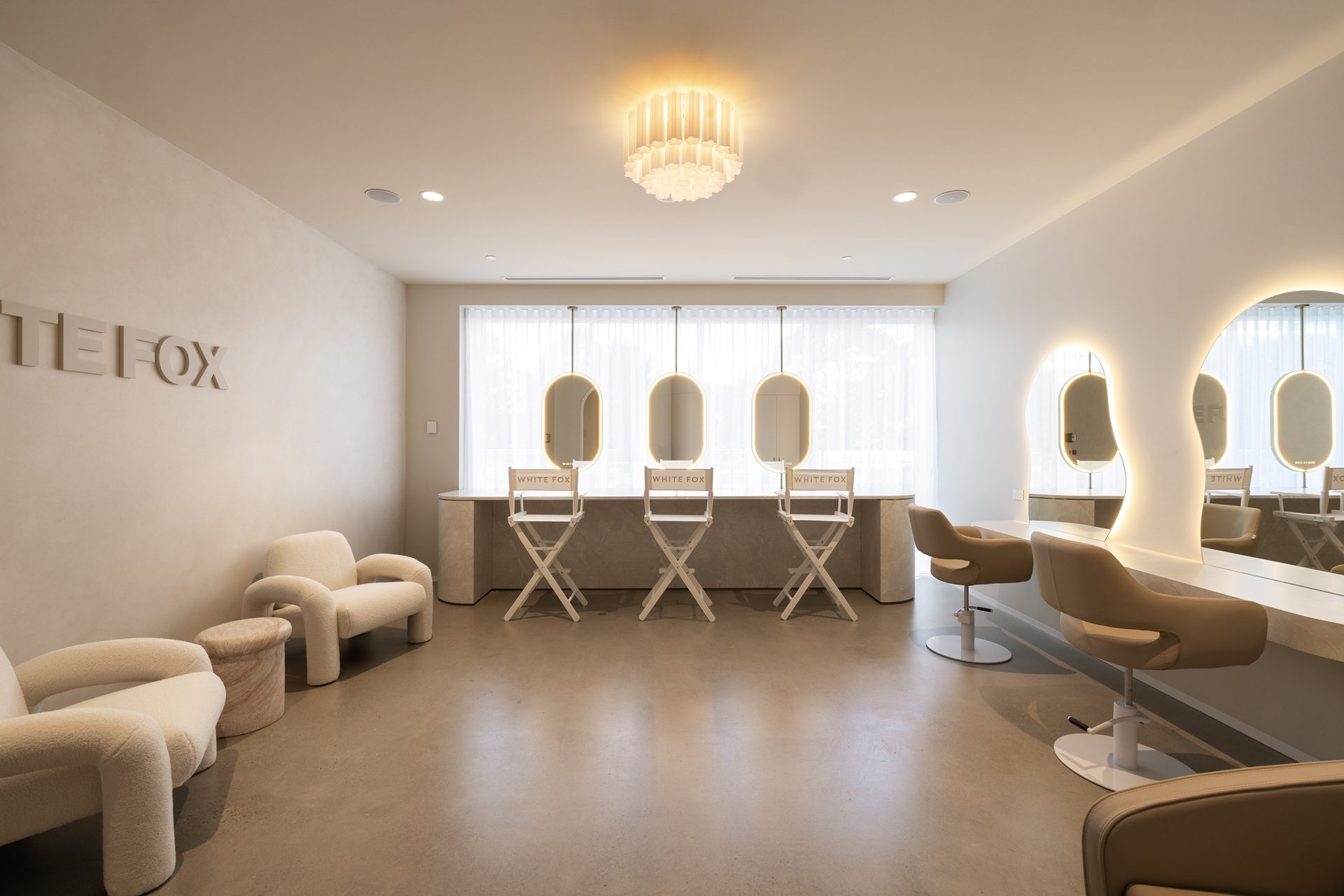The styling studio with three suspended pill mirrors over a bench and free-form backlit mirrors along the right-hand wall