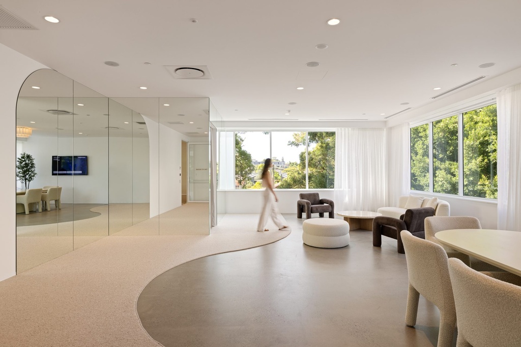 A bright lounge with a curved carpet path, armchairs and a full-height mirror wall with an arched end on the left