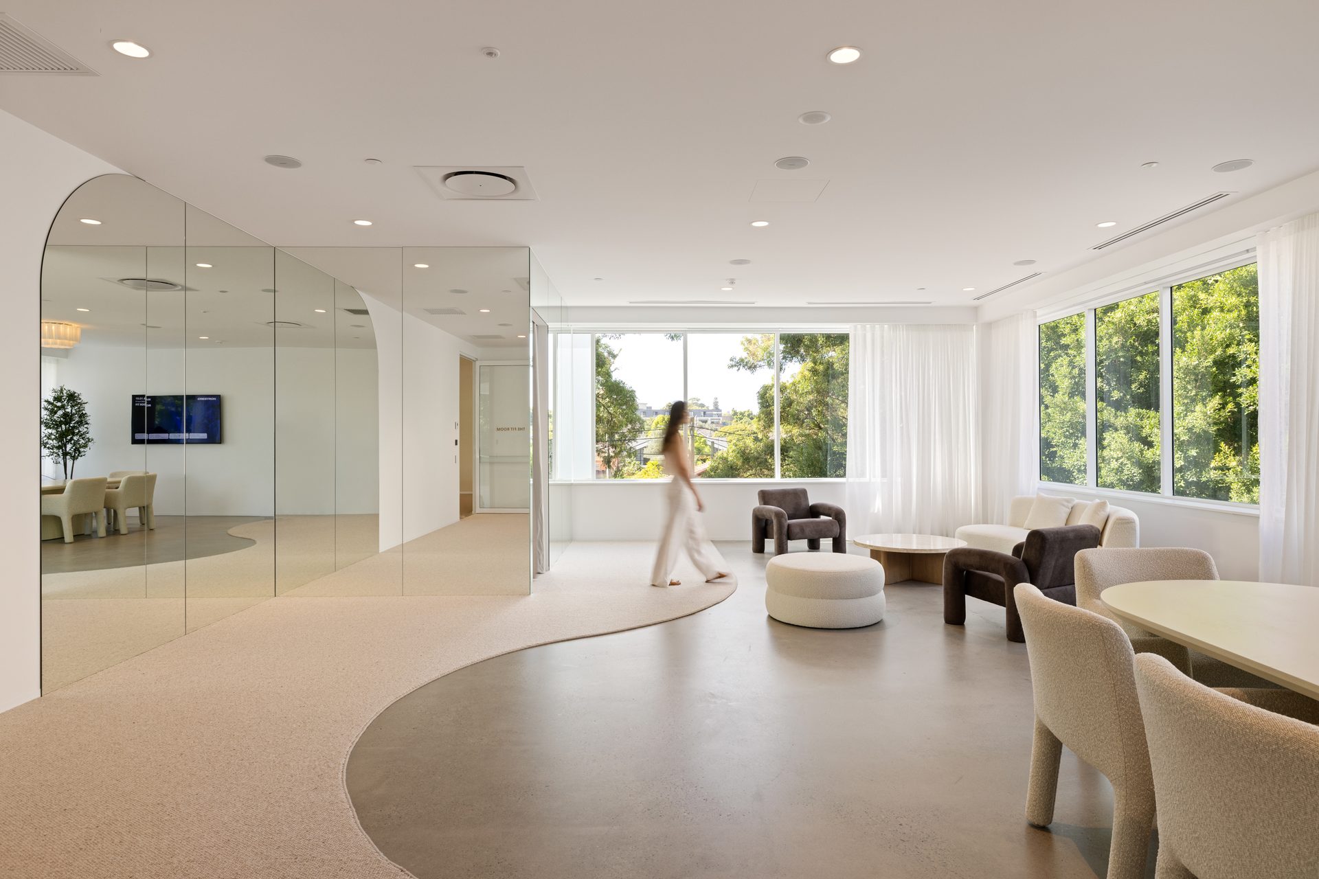 A bright lounge with a curved carpet path, armchairs and a full-height mirror wall with an arched end on the left