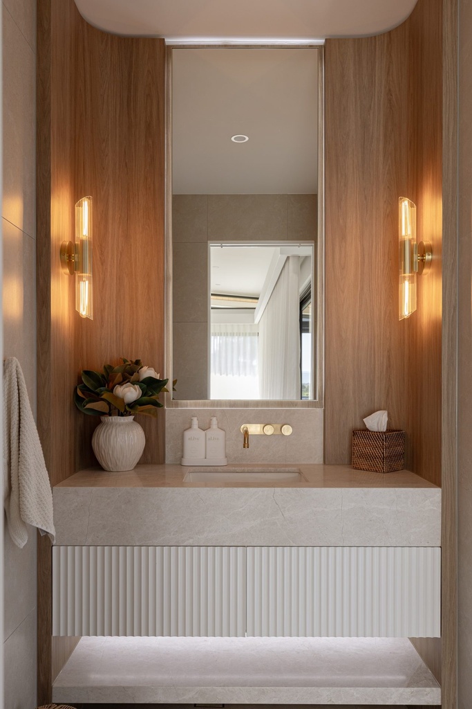 A powder room with a tall rectangular mirror in a timber-lined niche between two wall lights, above a stone basin