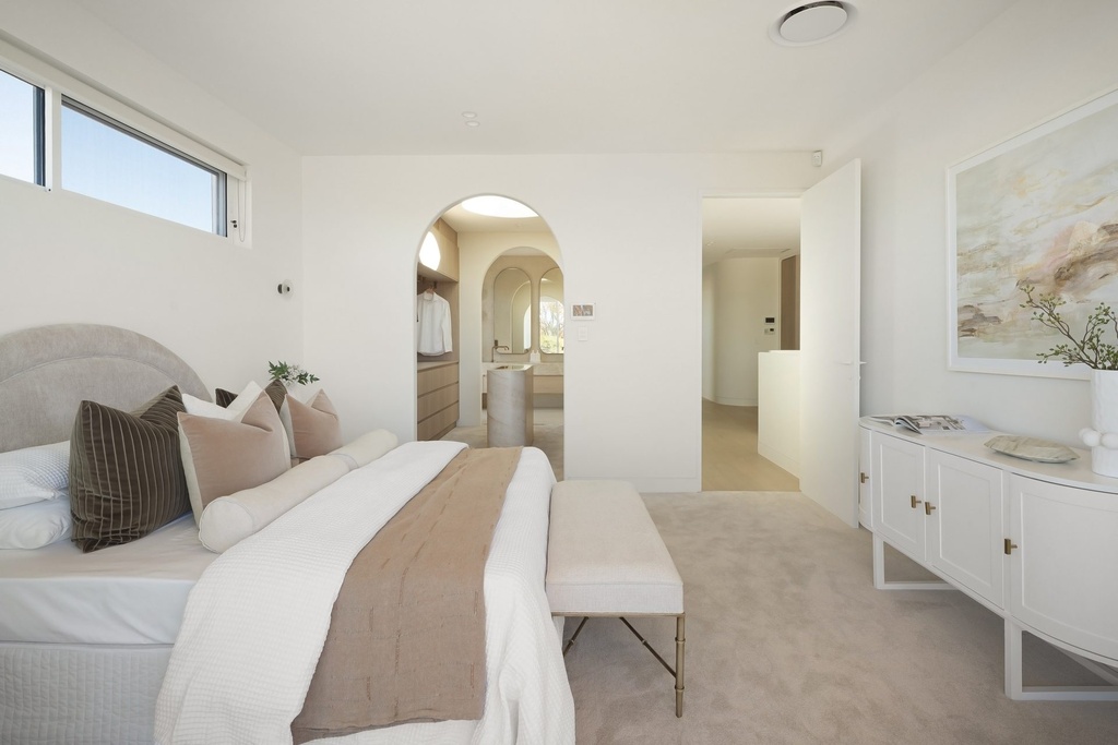 A bedroom with an upholstered bed and a large framed artwork, with an arched opening to the dressing room and ensuite