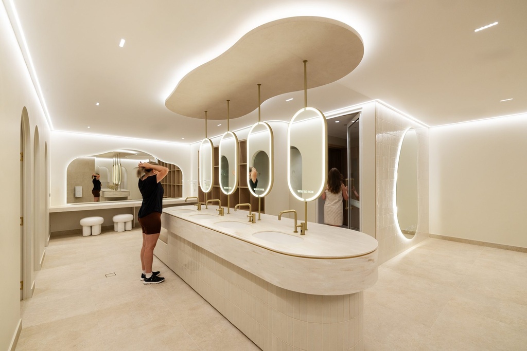 A vanity room with four pill-shaped backlit mirrors hung on rods from a curved ceiling over a long stone basin bench