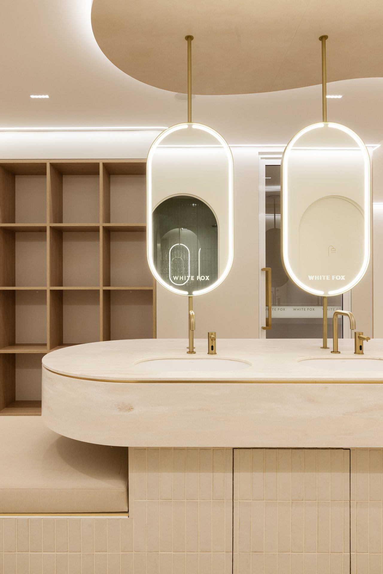 Two pill-shaped backlit mirrors in metal frames hung on rods above a stone vanity, each with the White Fox name in the glass