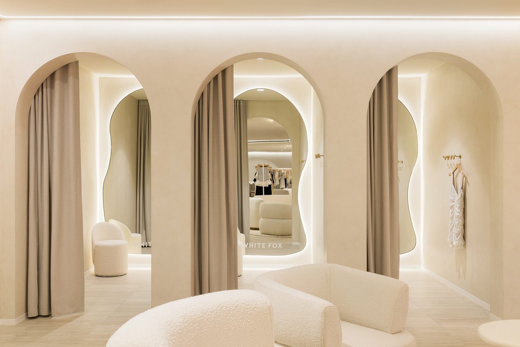 Three arched change room openings with curtains drawn back, each framing an organic-shaped backlit mirror, one with the White Fox name in the glass