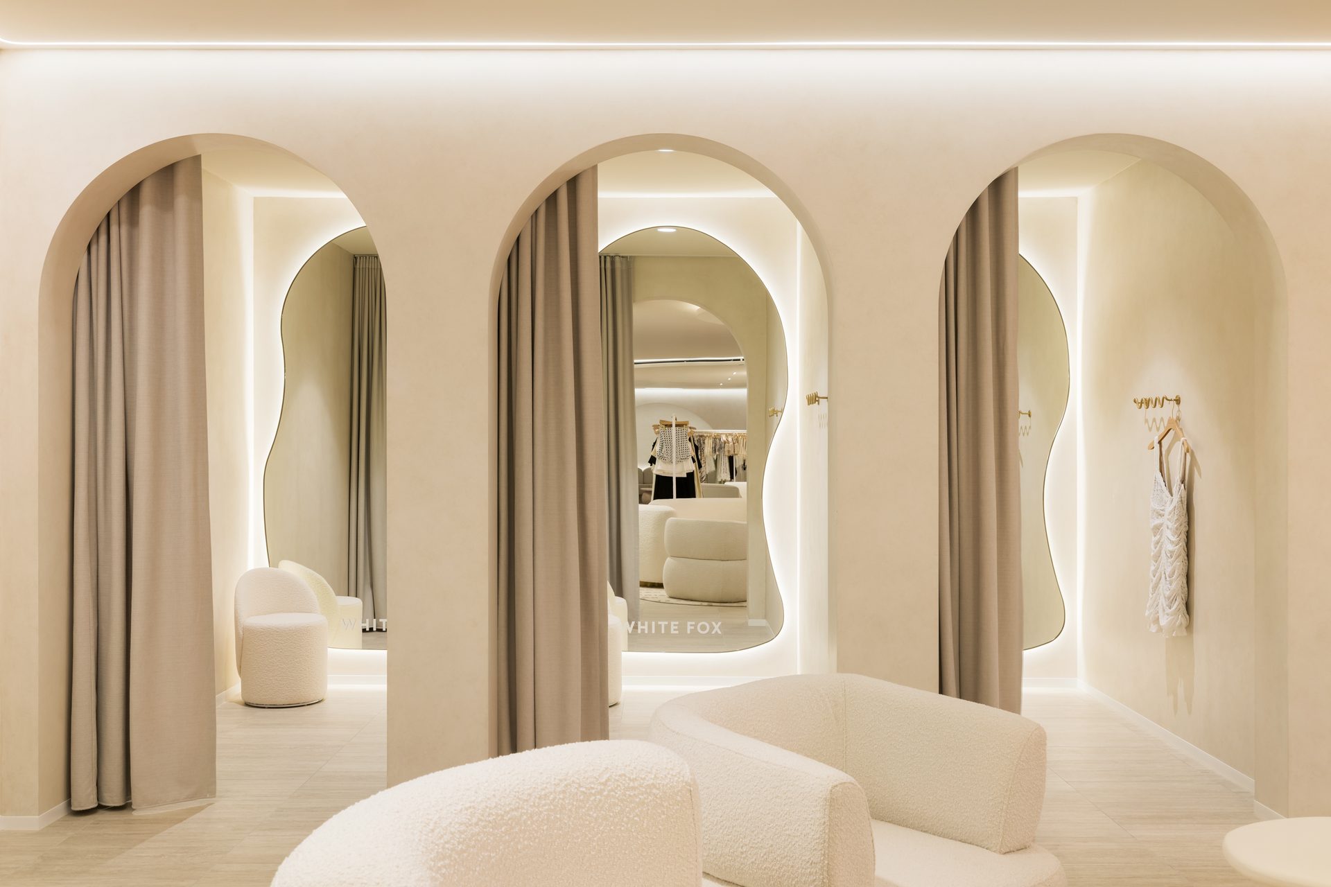 Three arched change room openings with curtains drawn back, each framing an organic-shaped backlit mirror, one with the White Fox name in the glass