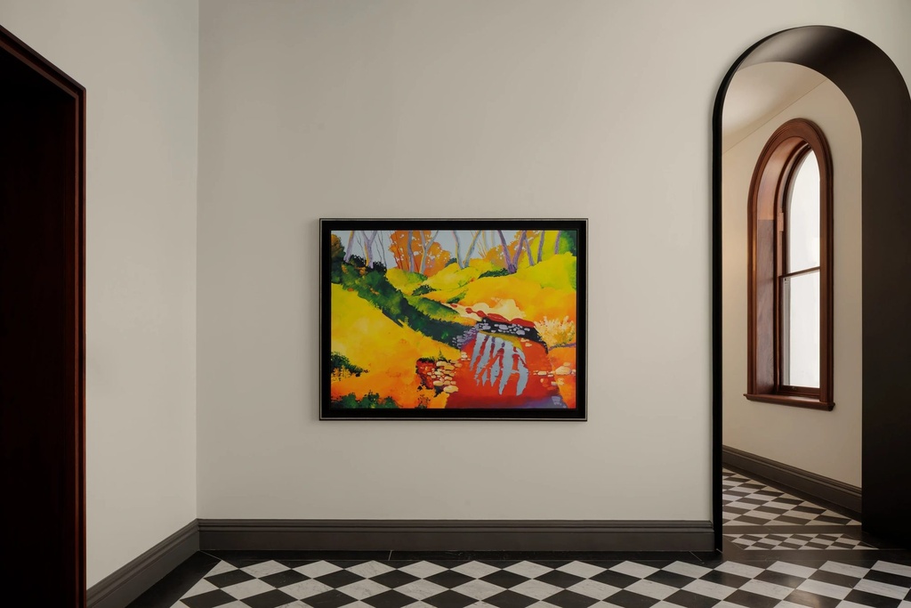Clare creek in winter by Marek Herburt, a bright yellow and red landscape painting in a dark frame, in a hallway with a chequered marble floor and an arched doorway
